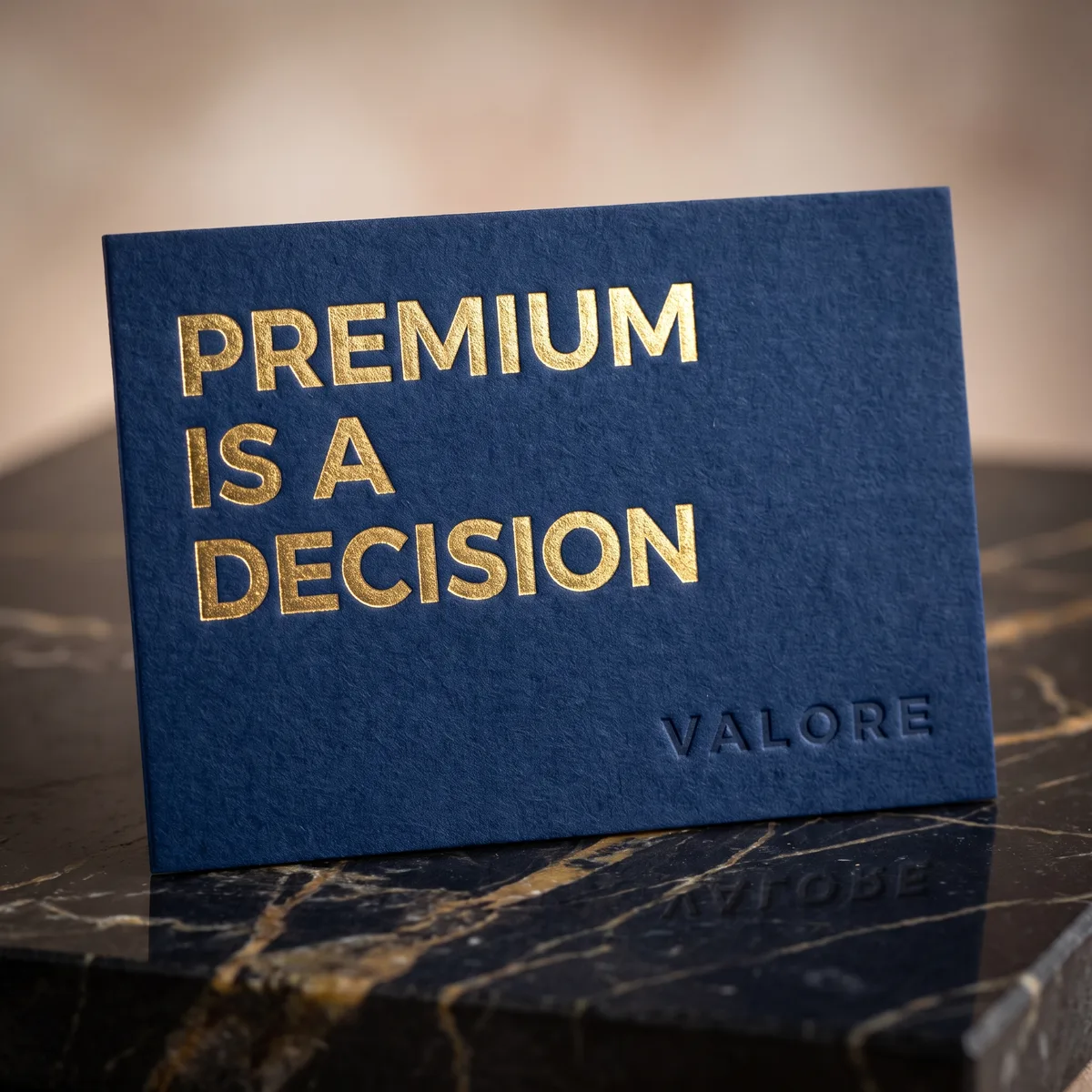 A navy card in gold foil reading Premium Is A Decision, on black marble, by Valore